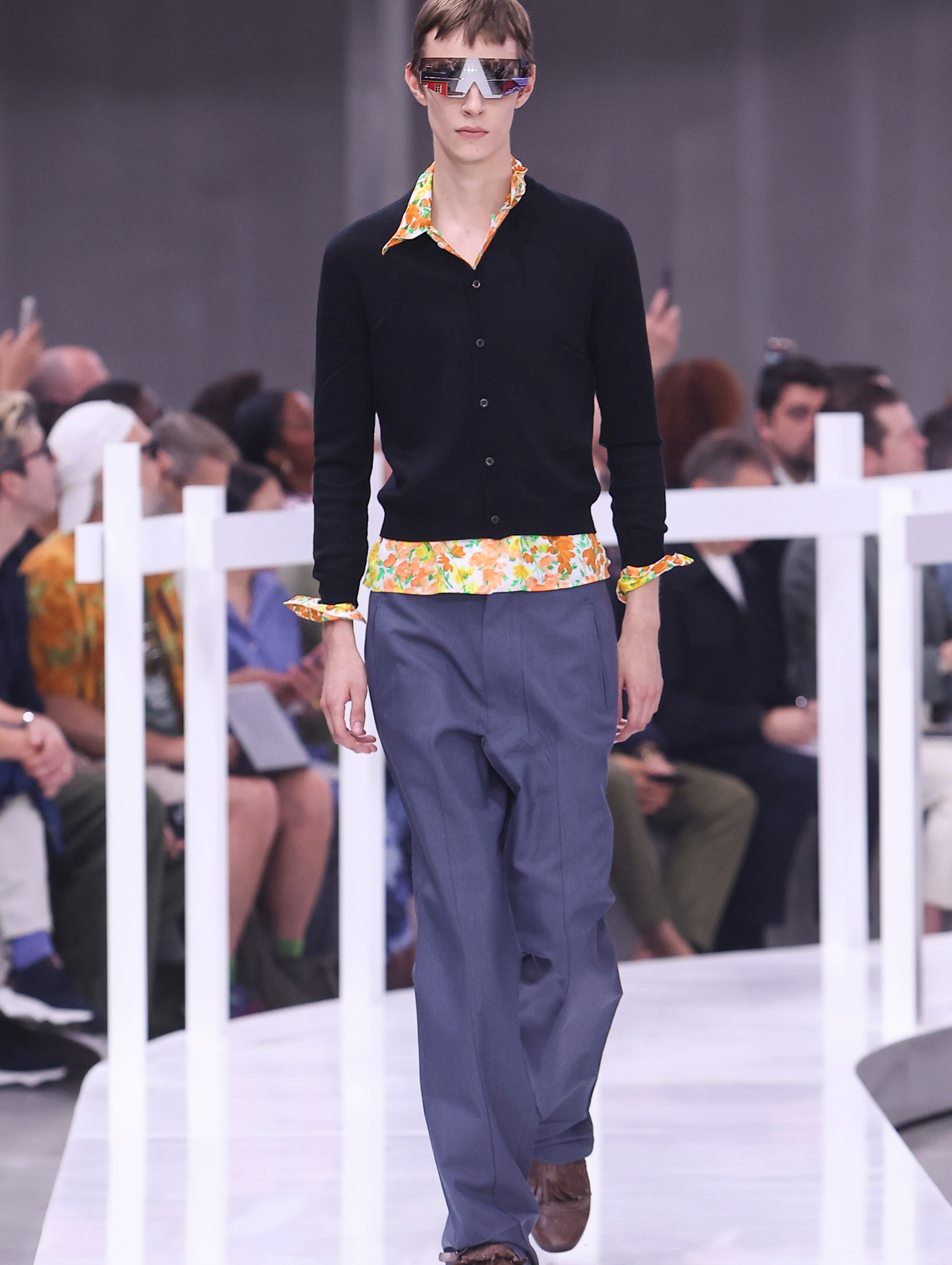 A model on the catwalk wearing a shrunken vintage-like floral shirt with deformed collars and hems 